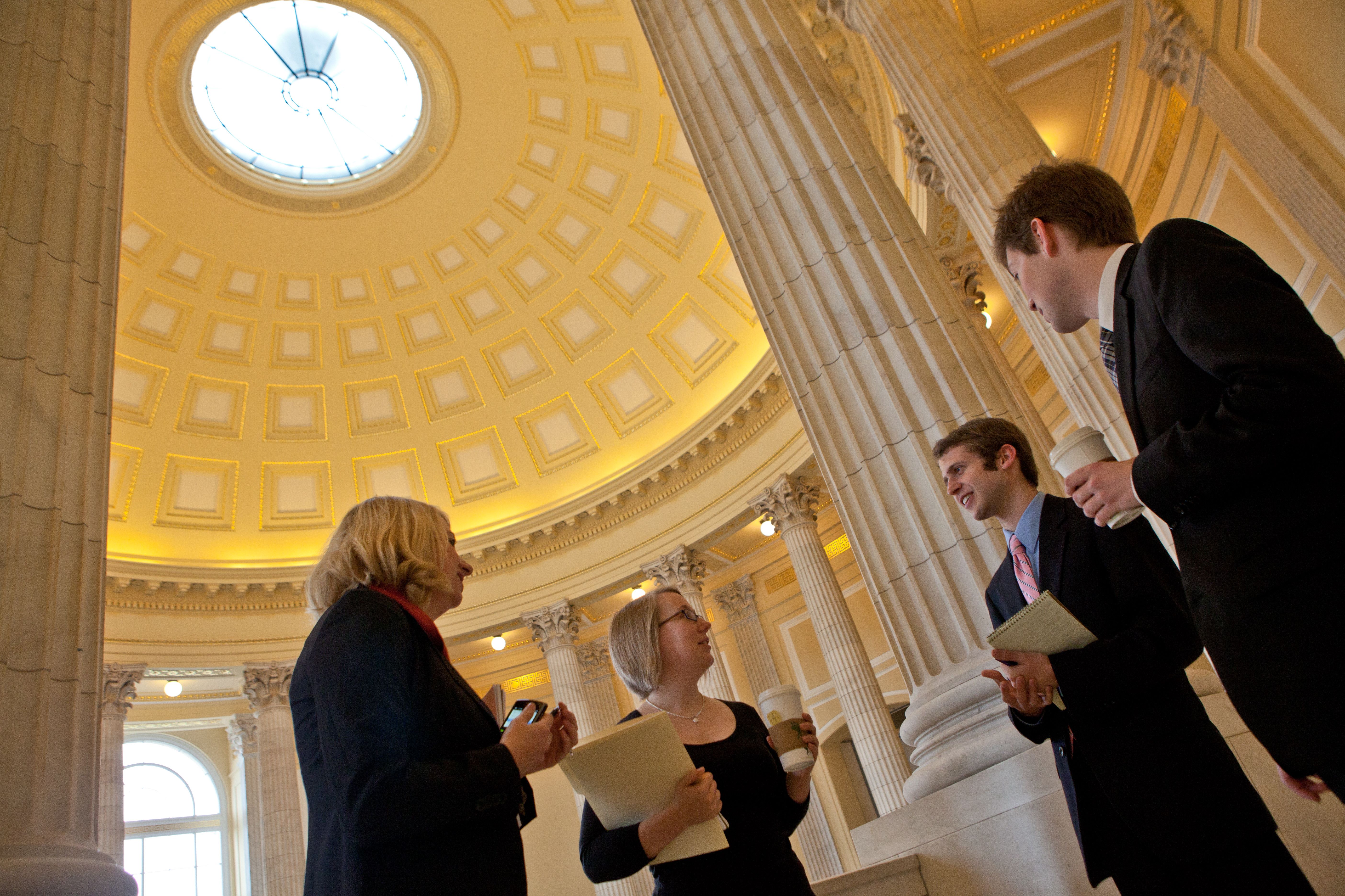 Four people standing and speaking to each other under a rotunda