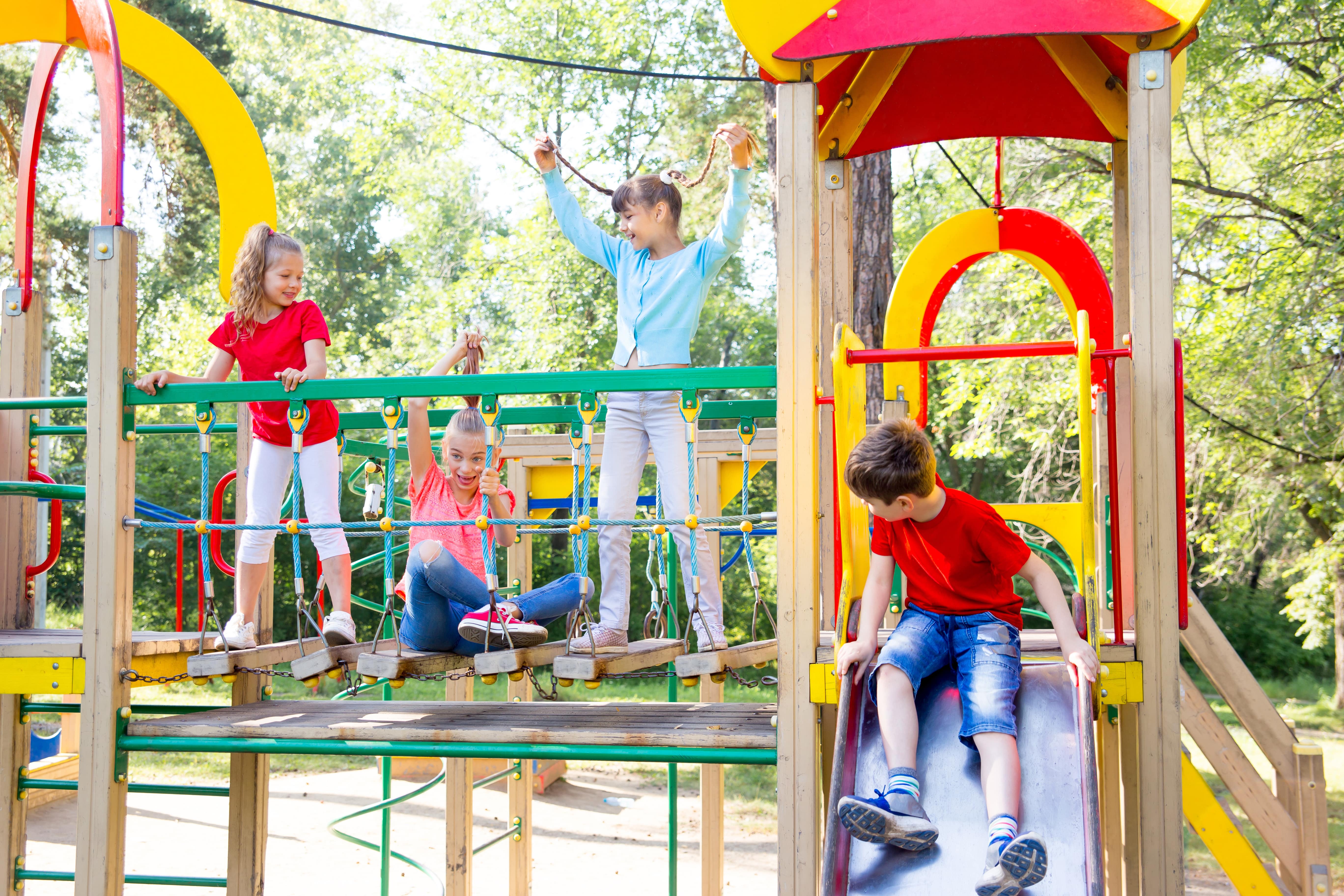 Children playing on a colorful playground with trees in the background.