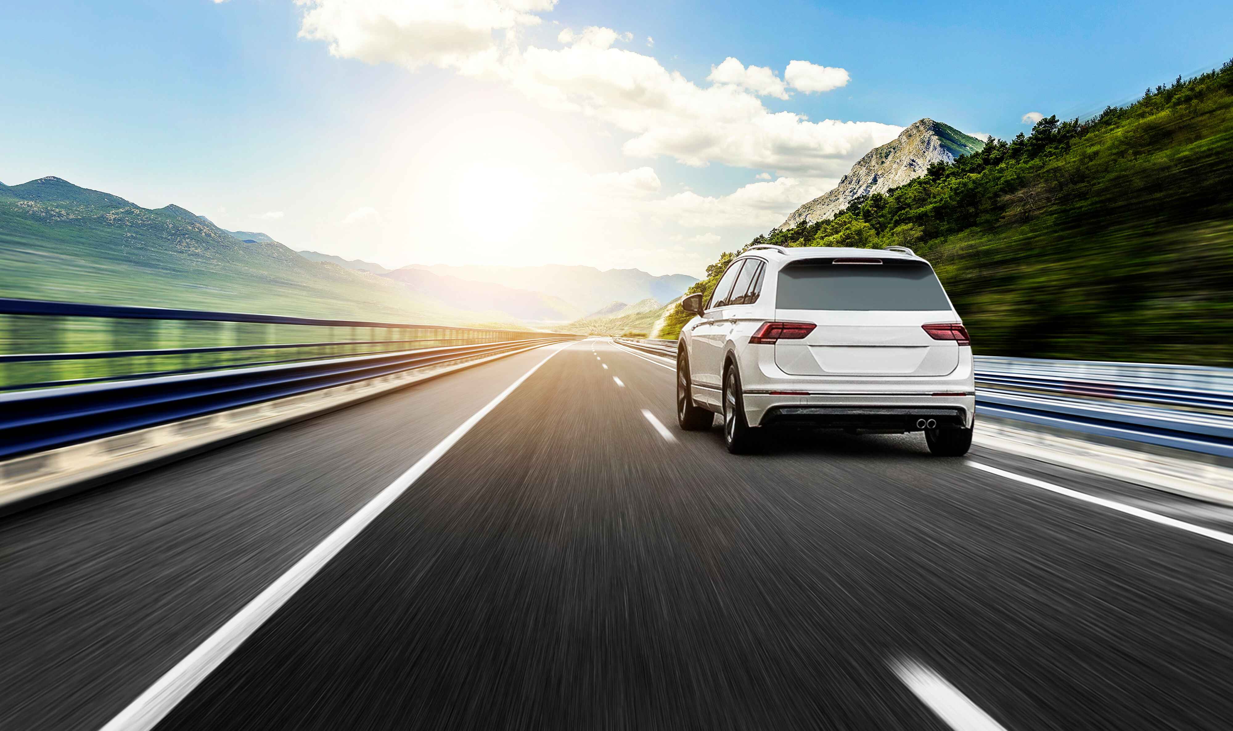 A white SUV driving on a sunny highway with mountain scenery.