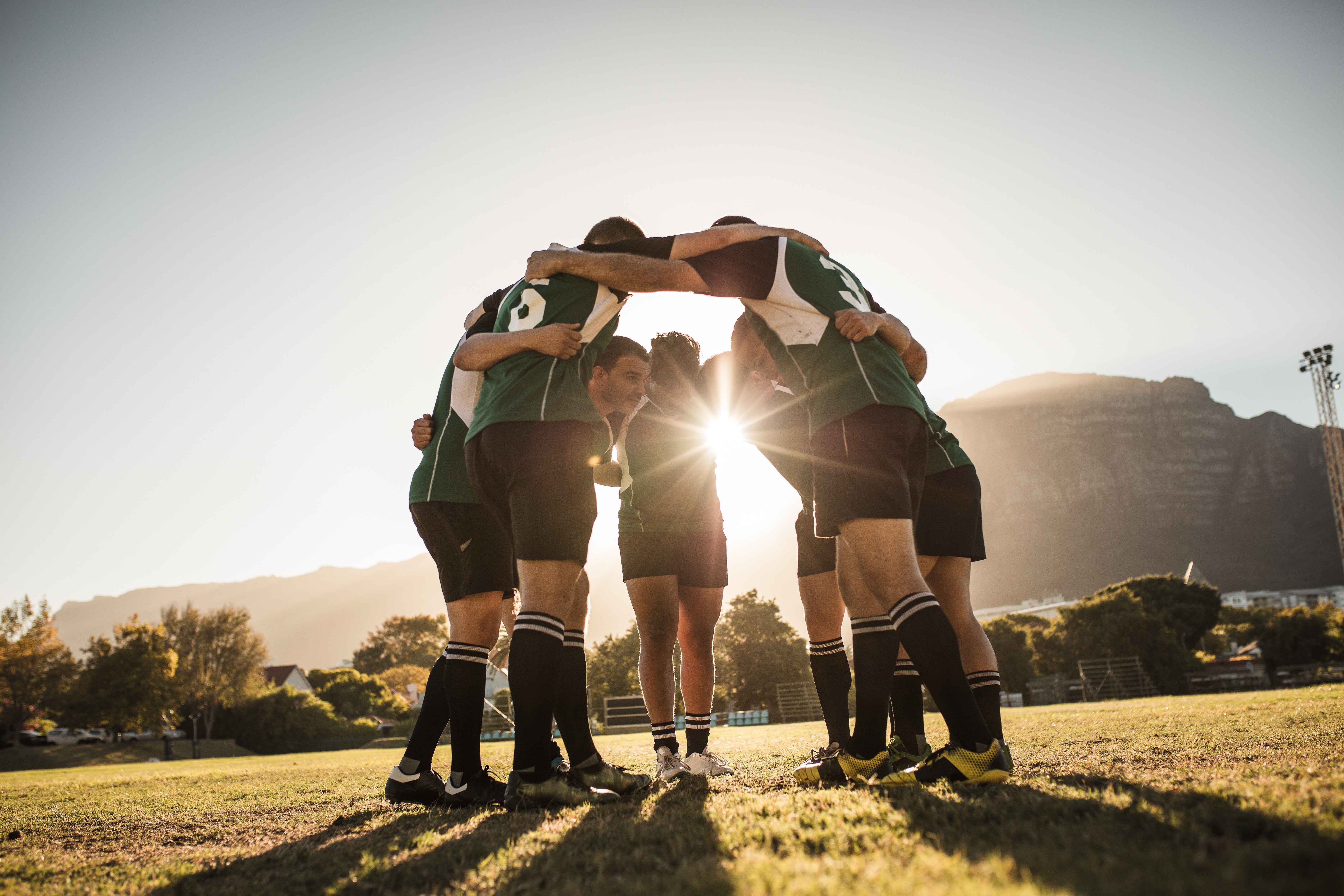 A group of soccer athletes huddled together on a field with the sun setting behind them.