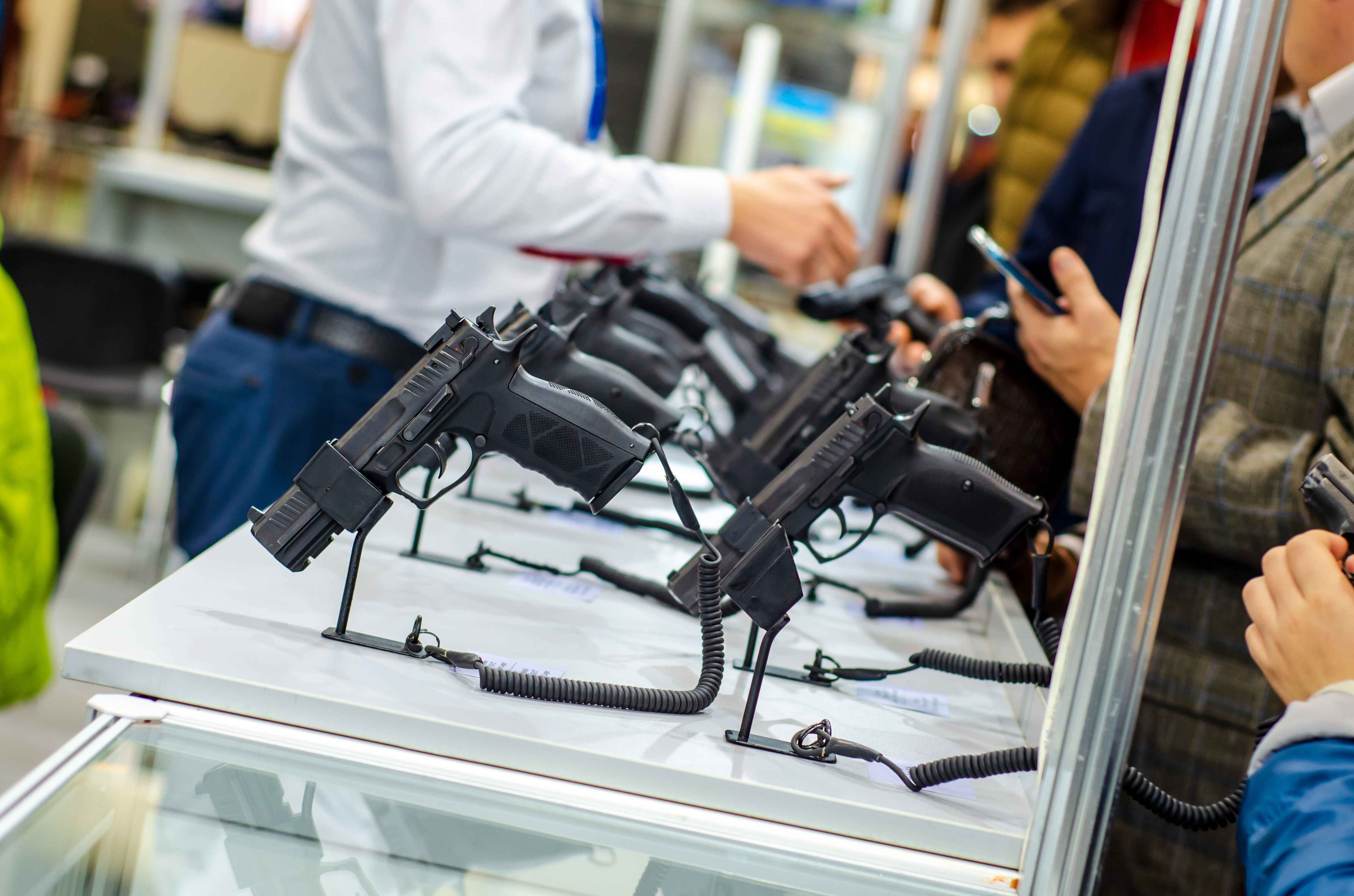 Display of black handguns on a counter with people examining them.