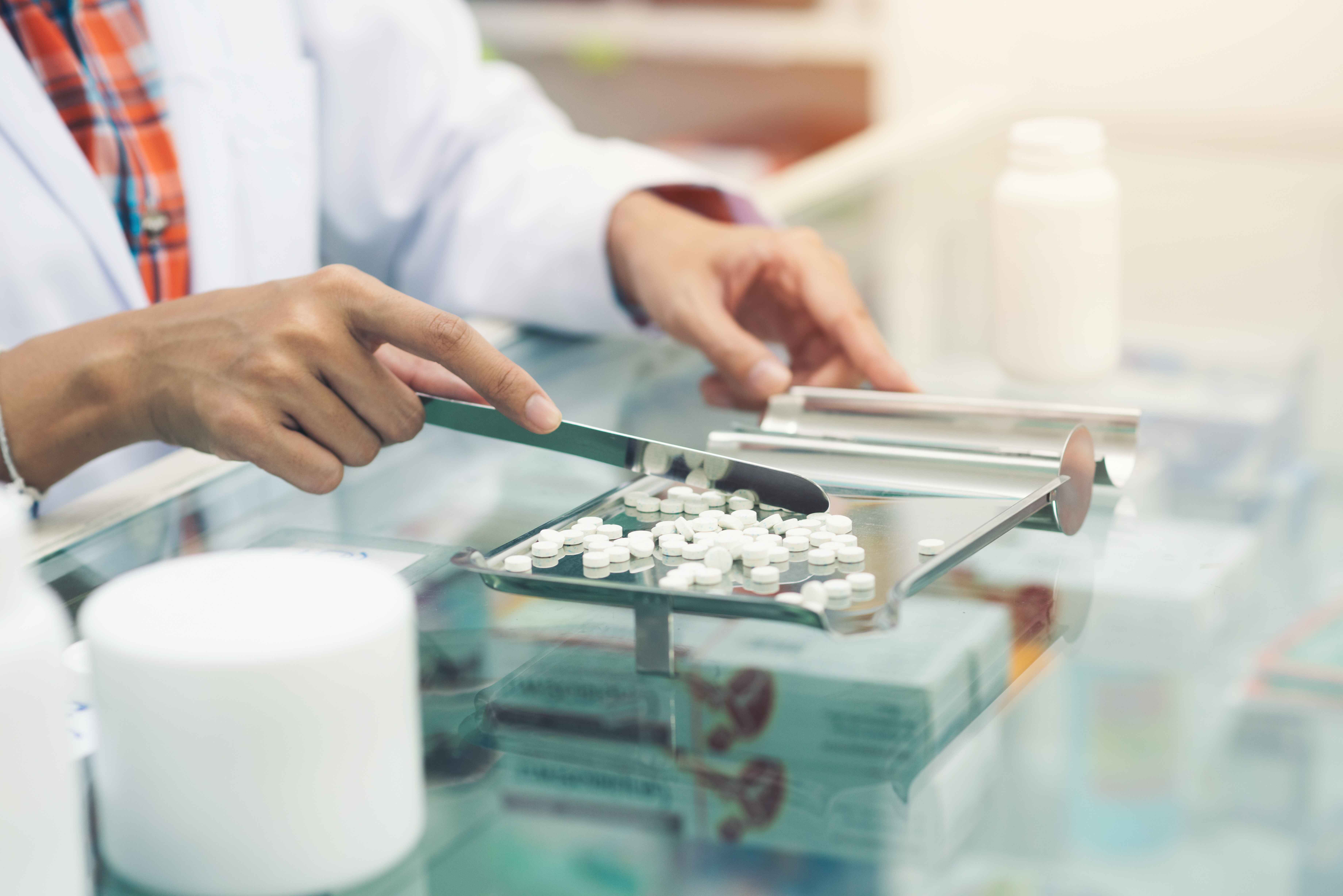 Pharmacist sorting white pills on a metal tray with a spatula.