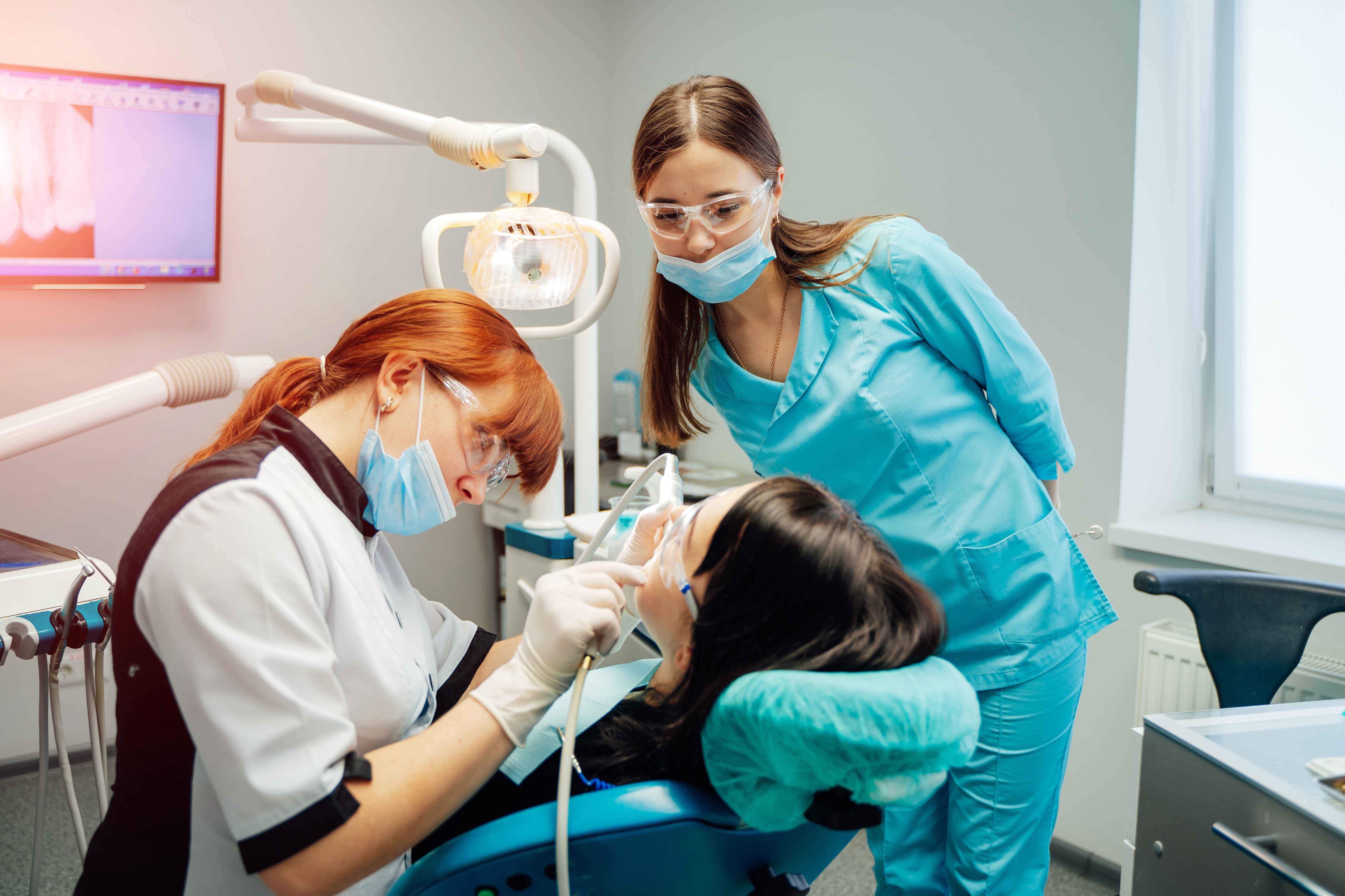 A dentist and assistant perform a dental procedure on a patient in a dental clinic.