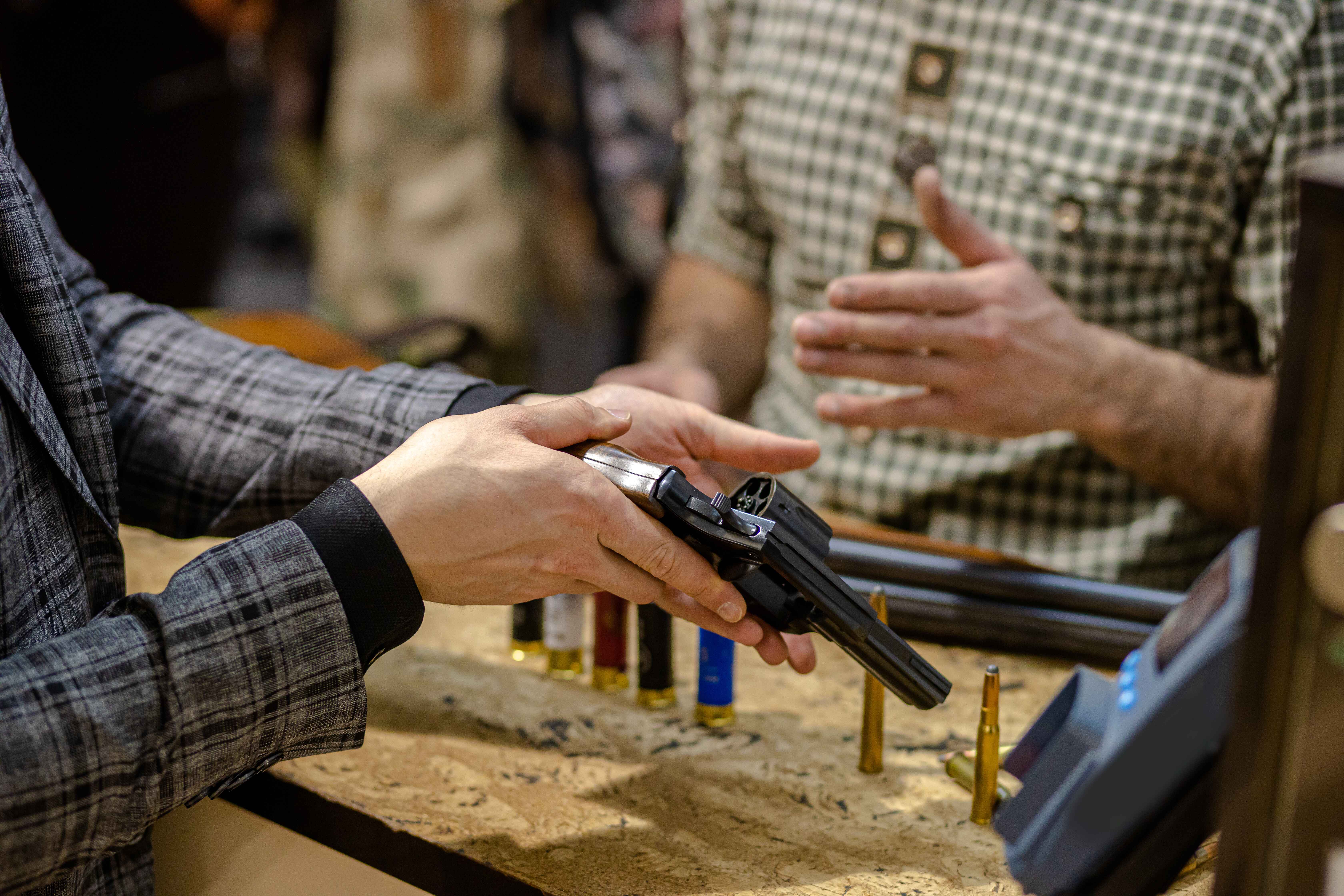 A person in a plaid jacket holds a revolver over a counter with bullets.