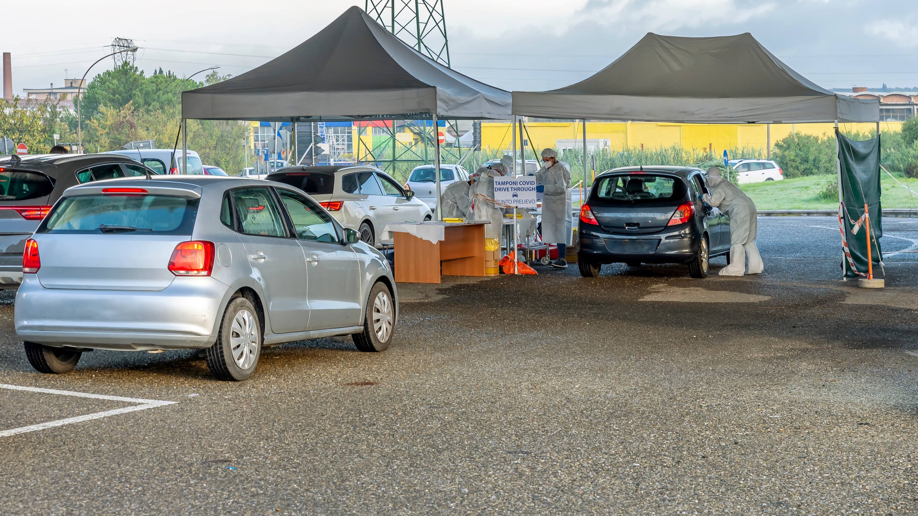 Drive-through COVID-19 testing site with cars under tents and personnel in protective gear.