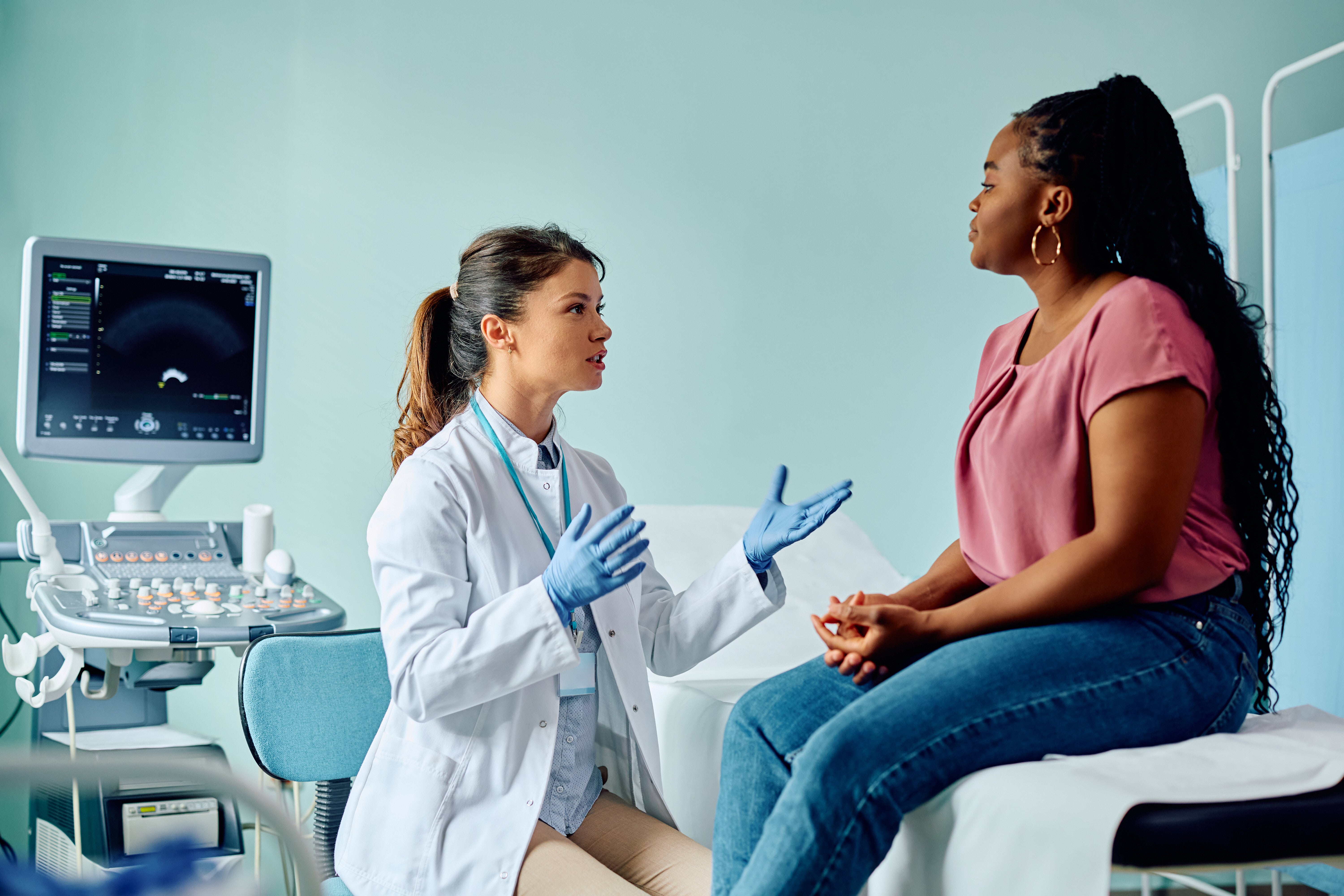 A healthcare professional in a white coat consults with a patient on an examination table near an ultrasound machine.