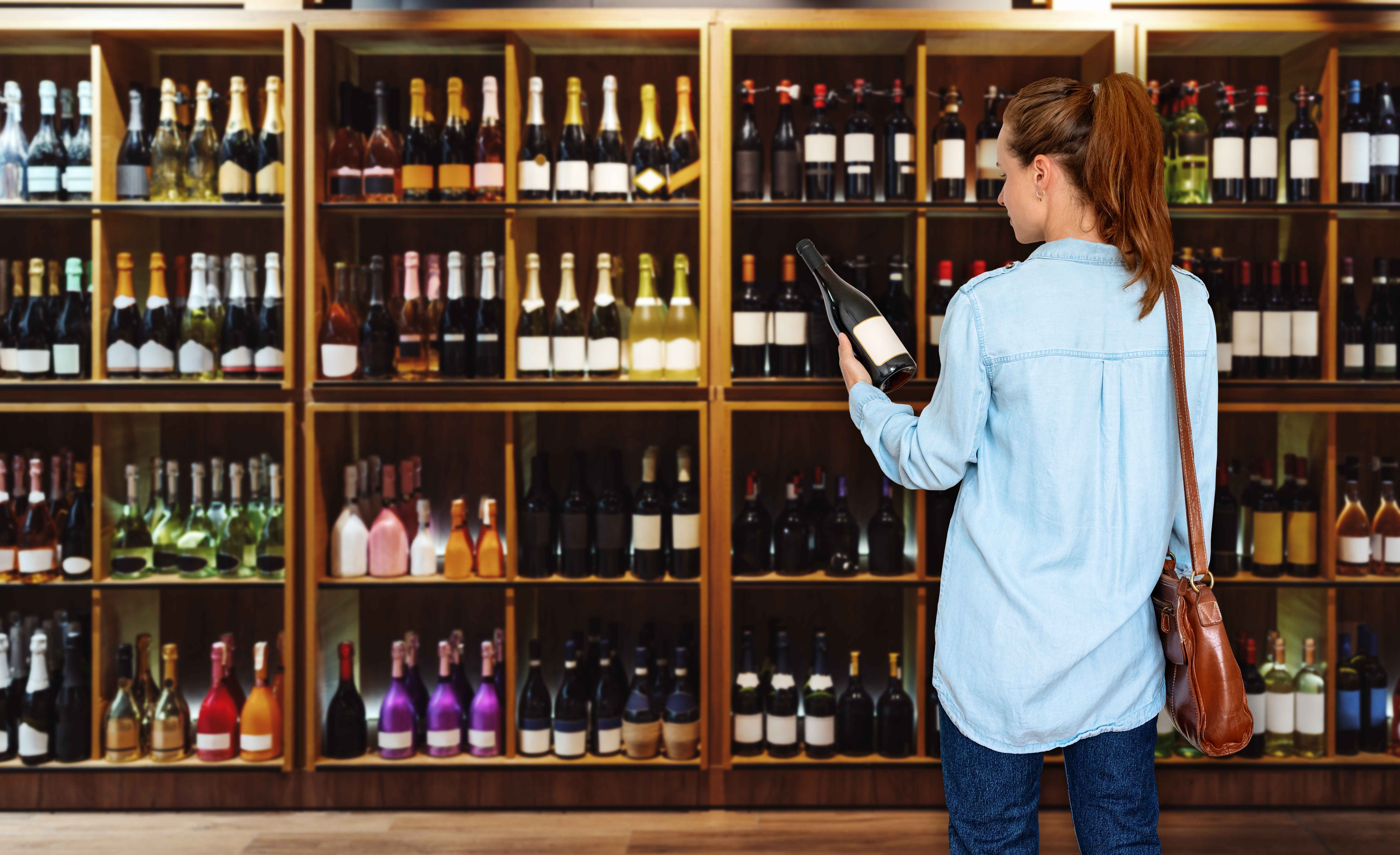 Woman browsing wine bottles on wooden shelves in a store.