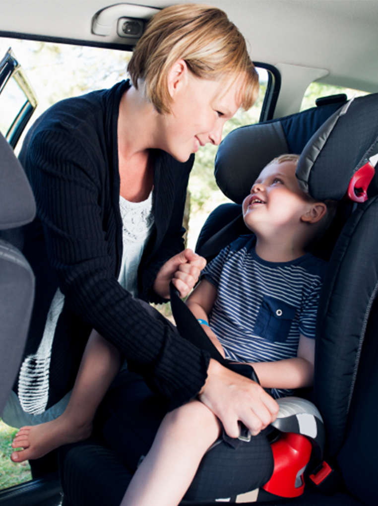 Adult helping a child in a car seat inside a vehicle.