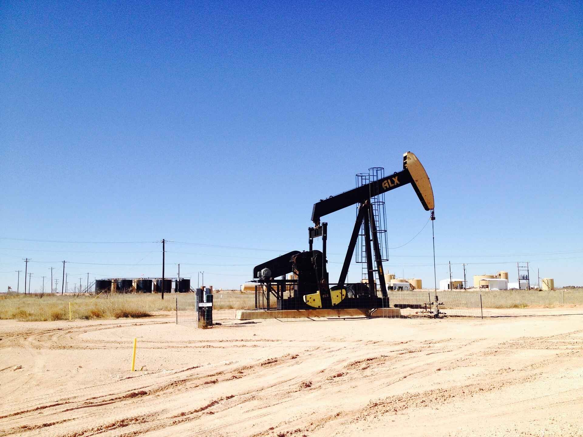 An oil pumpjack in a dry landscape with oil tanks and a clear blue sky.