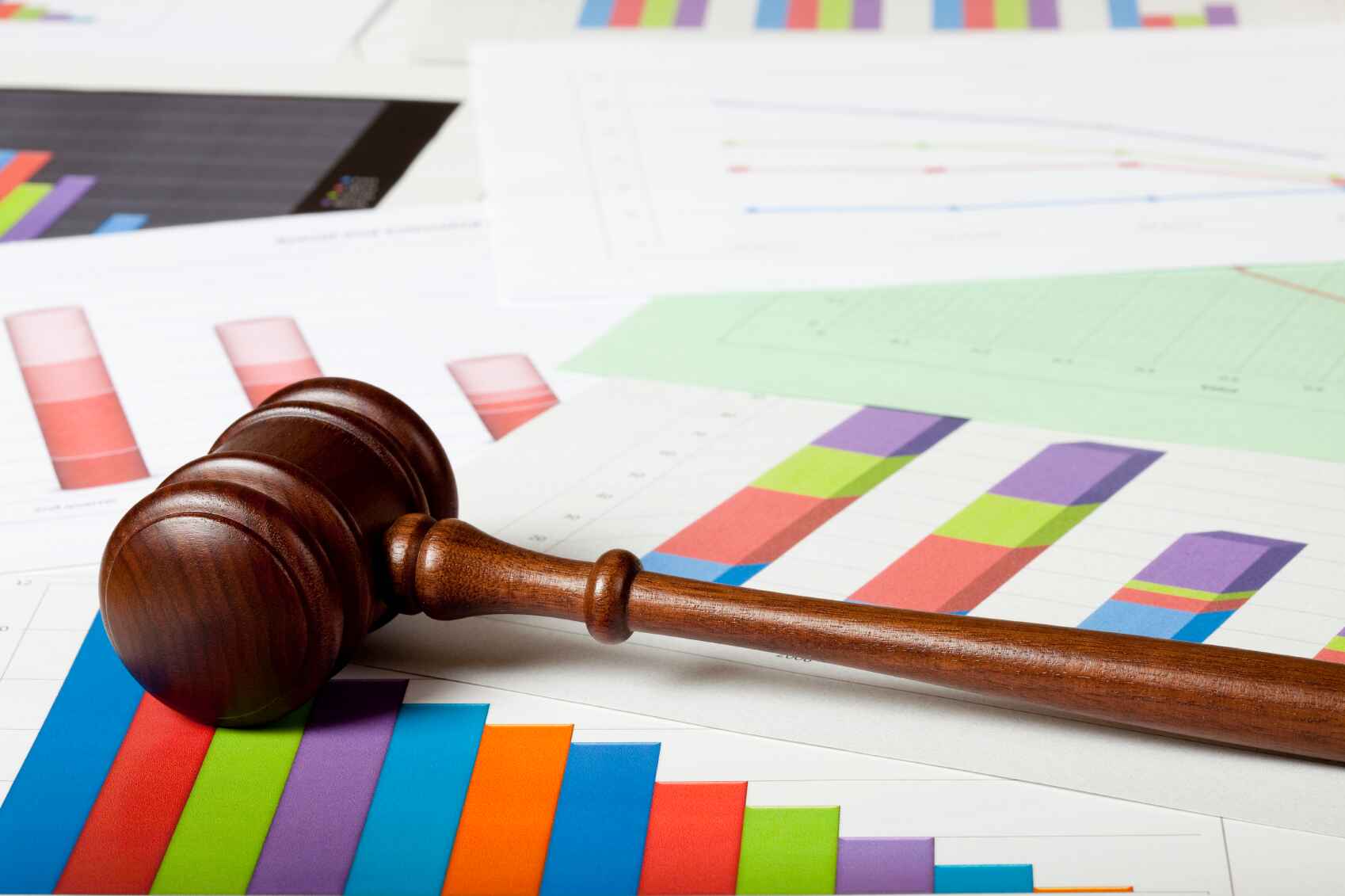 A wooden gavel resting on multicolored bar charts and graphs.