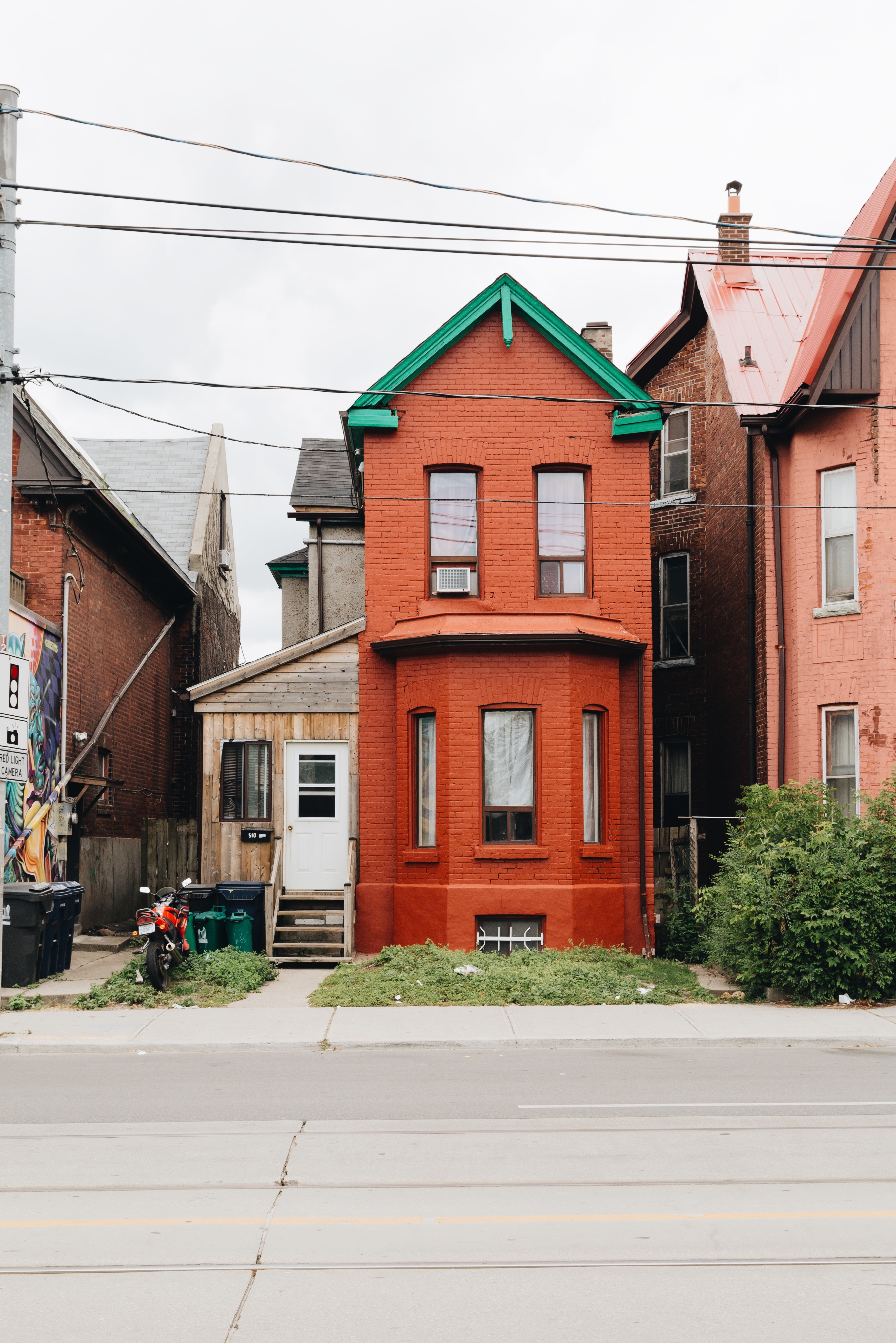 A red brick house with green roof accents and a white door, flanked by similar buildings.