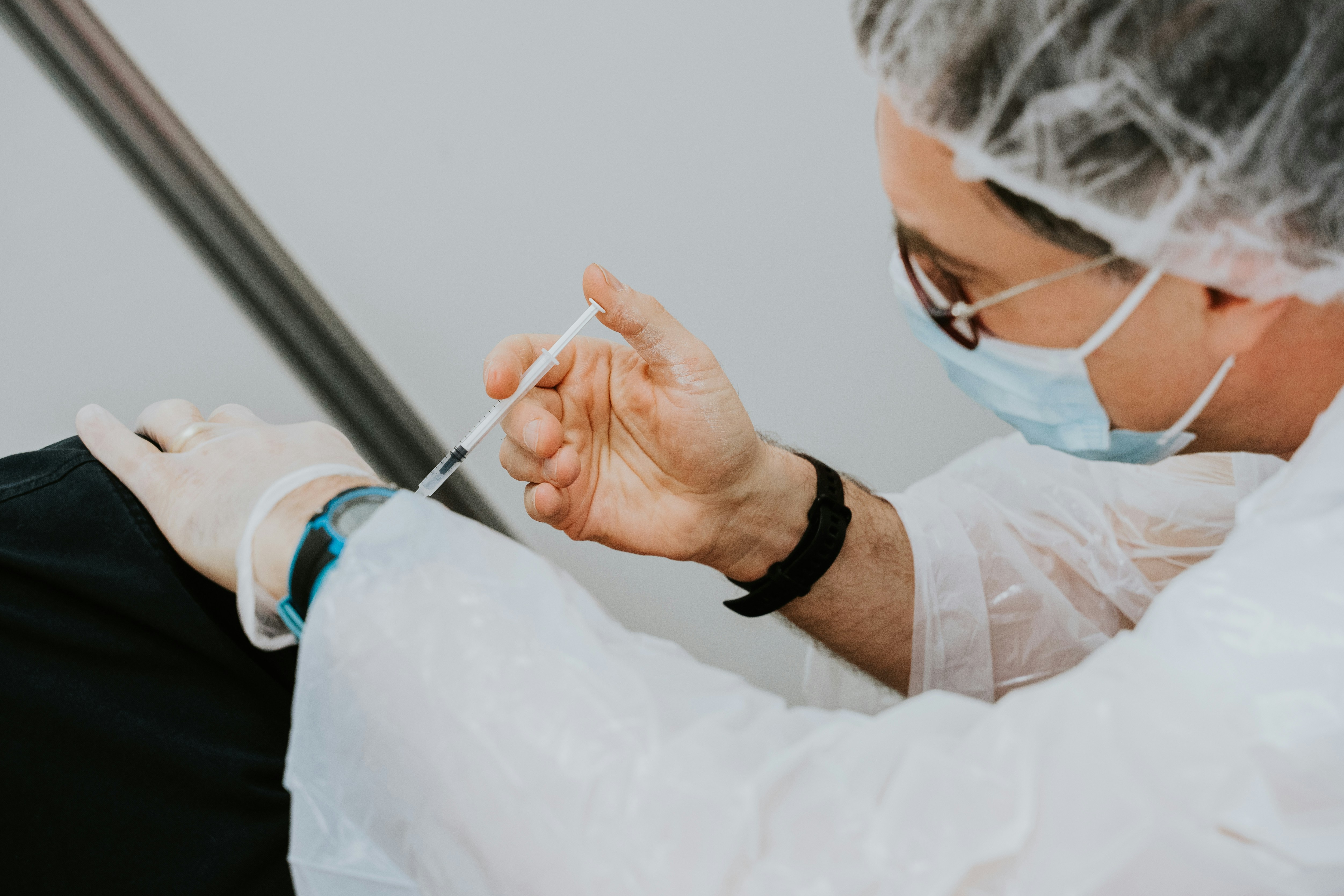 A person in protective gear administers an injection to a person out of frame