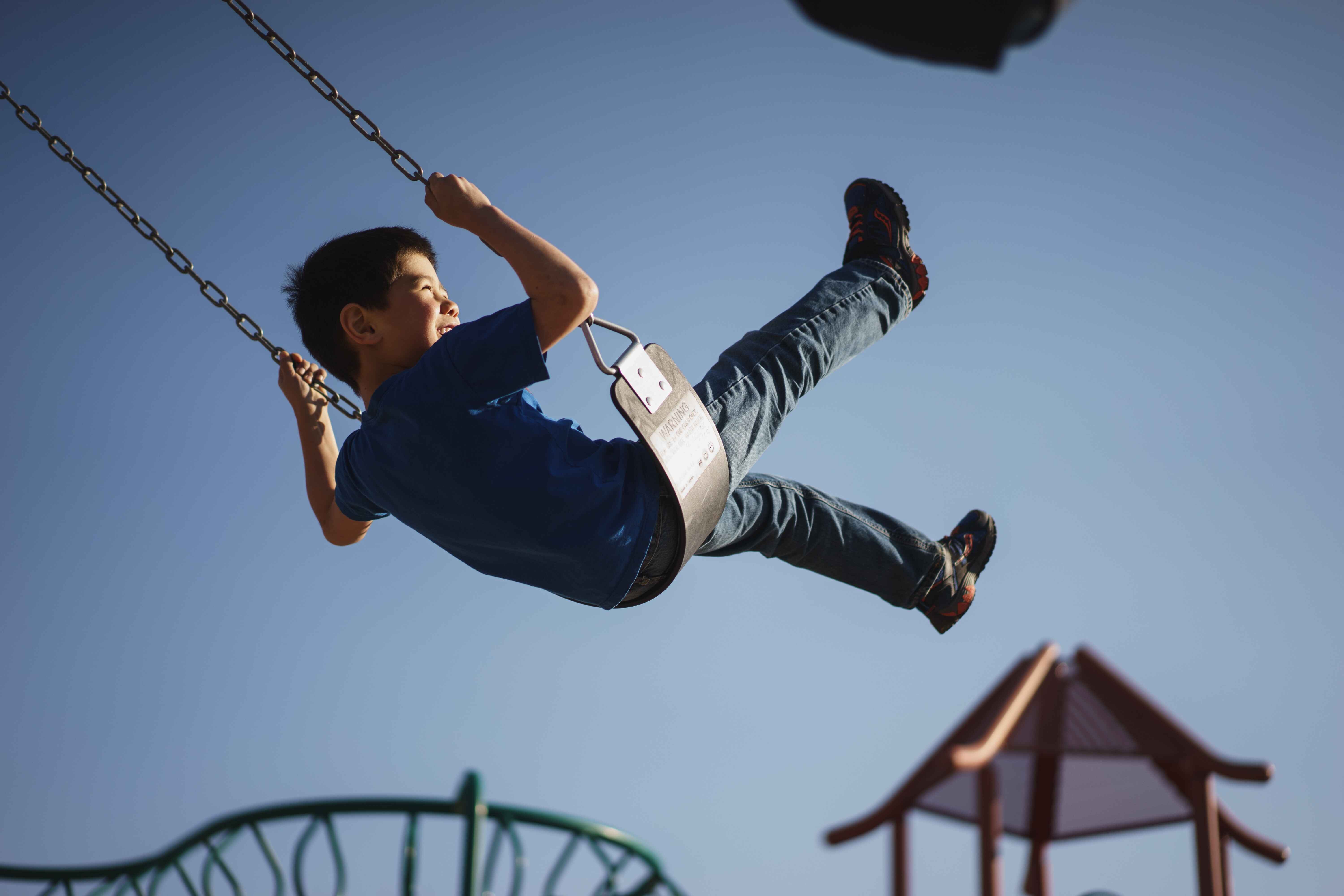 Boy swinging against a clear blue sky at a playground.