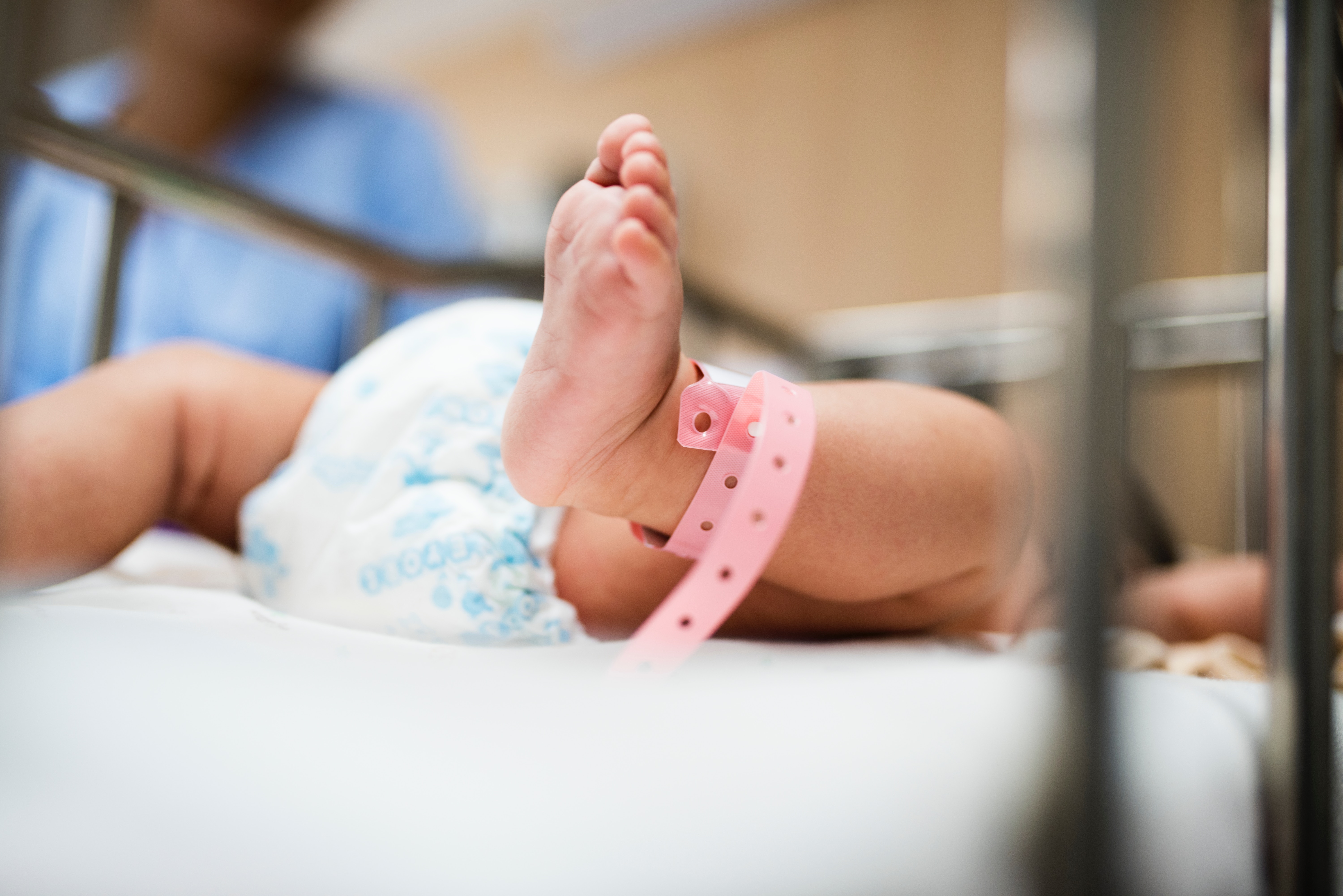 Close-up of a newborn's feet with a pink hospital ID band in a crib.