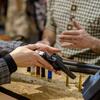 A person in a plaid jacket holds a revolver over a counter with bullets.
